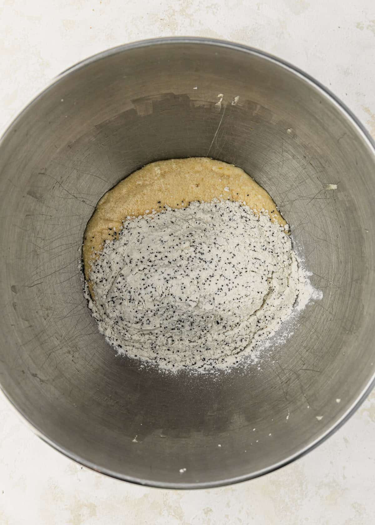 A silver bowl of flour and poppy seeds on a beige table.