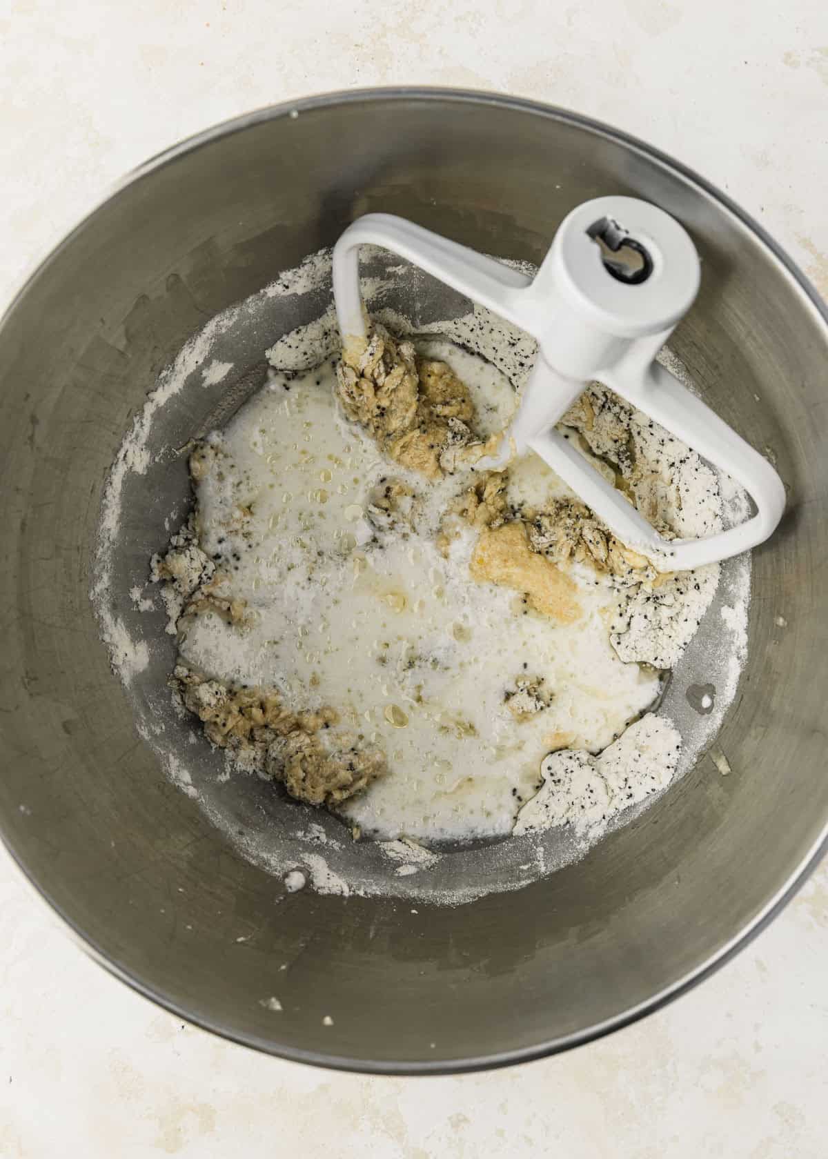 A silver bowl of batter and milk for small batch lemon poppy seed cupcakes.
