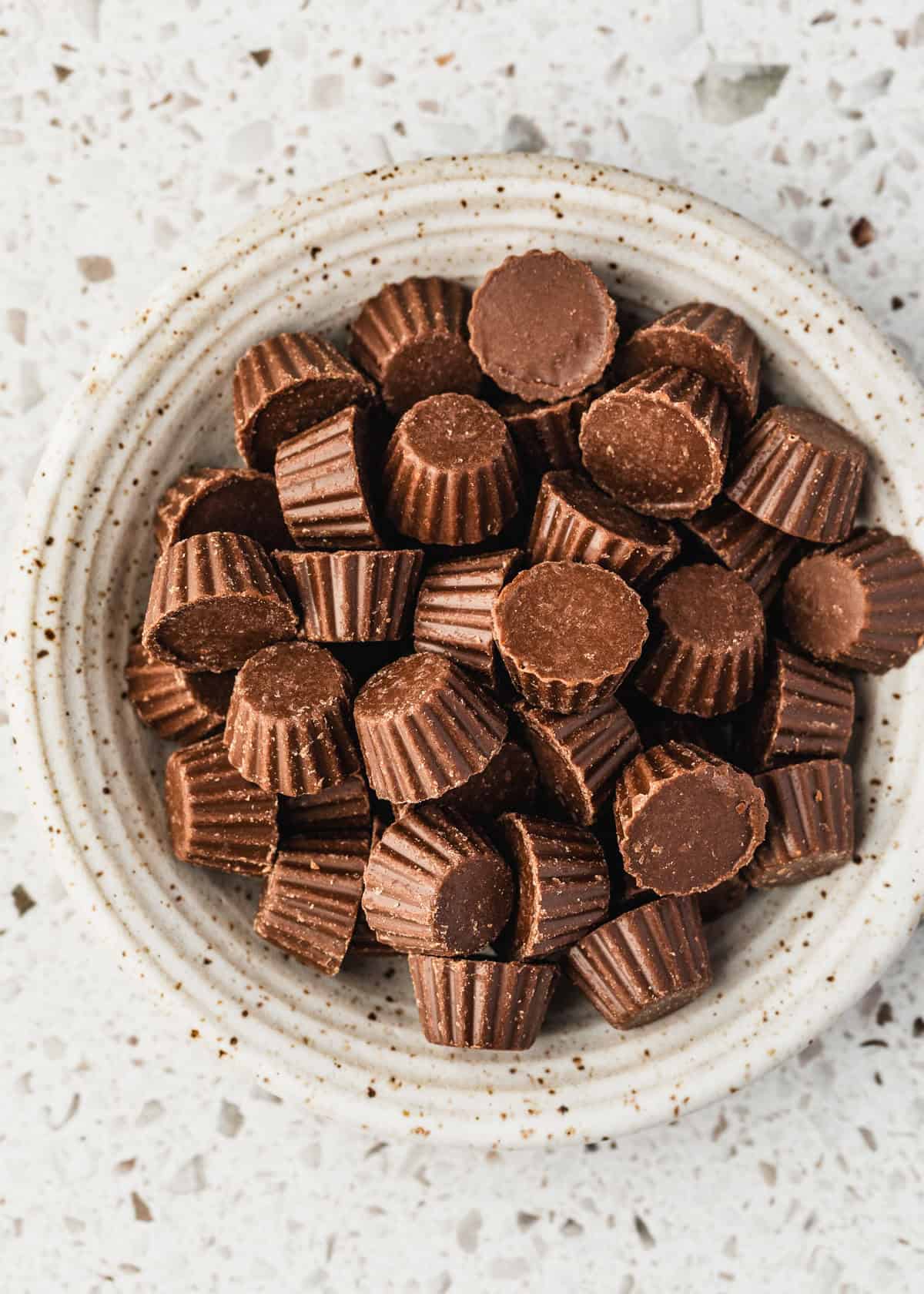 A white bowl of mini peanut butter cups on a white counter.