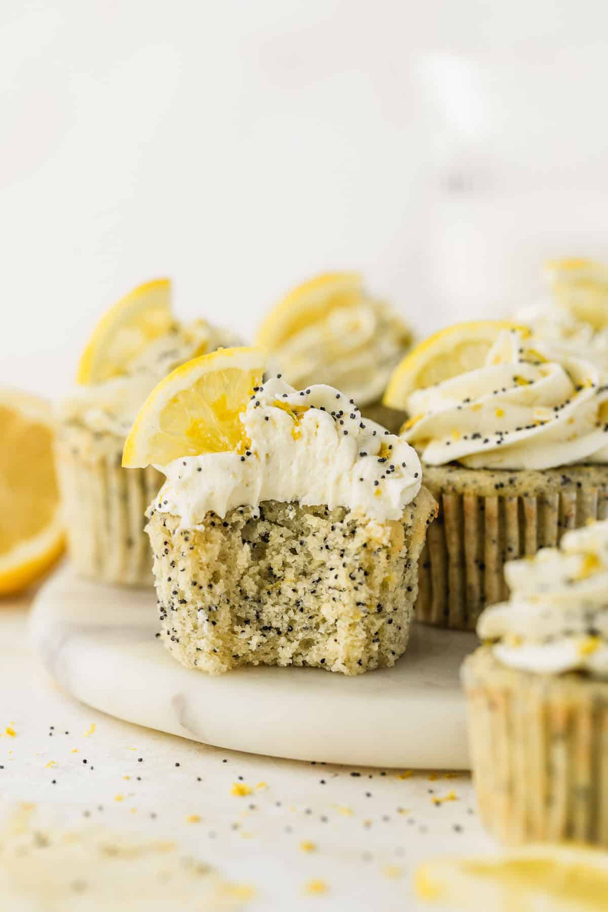 Small batch cupcakes with lemon buttercream on a white tray next to sliced lemons on a white background.