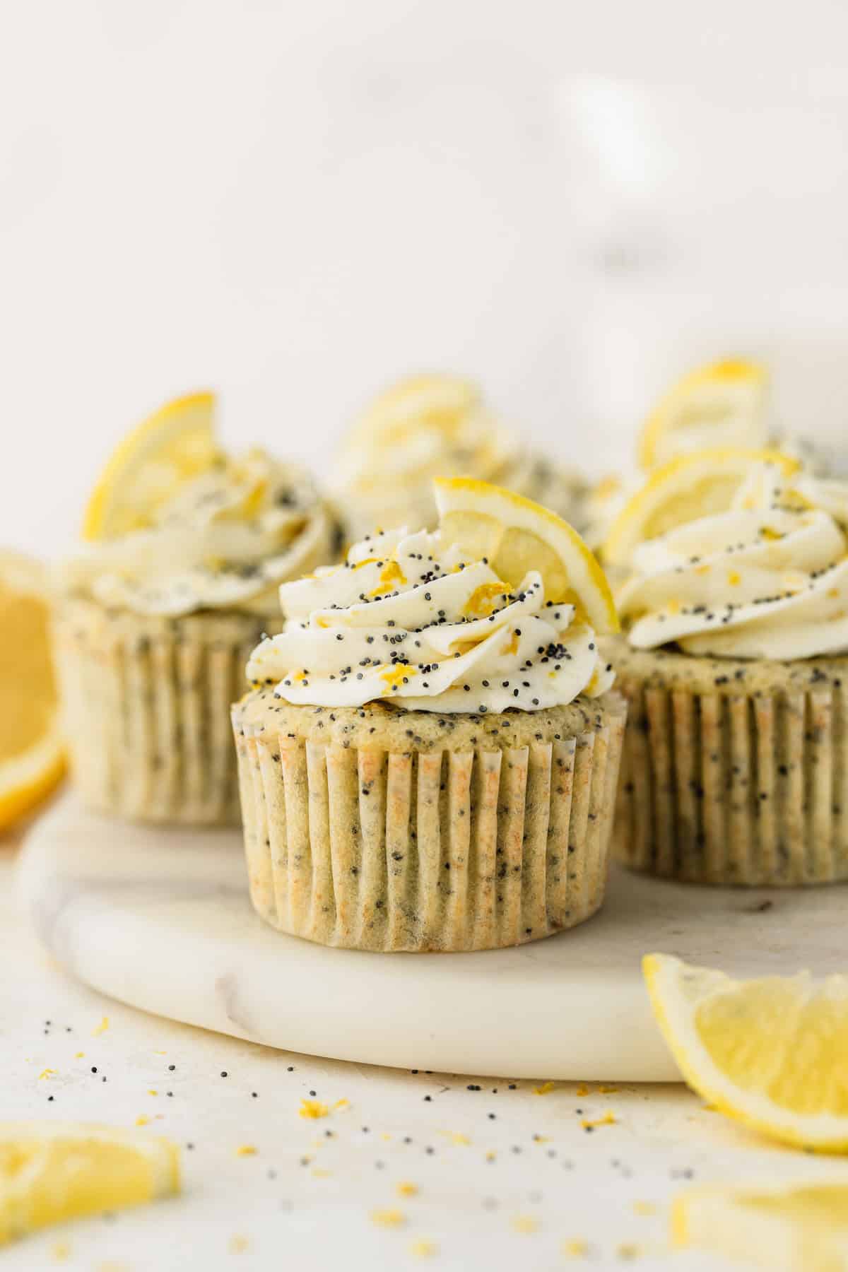 A white platter of small batch lemon poppy seed cupcakes next to lemon slices on a white backdrop.