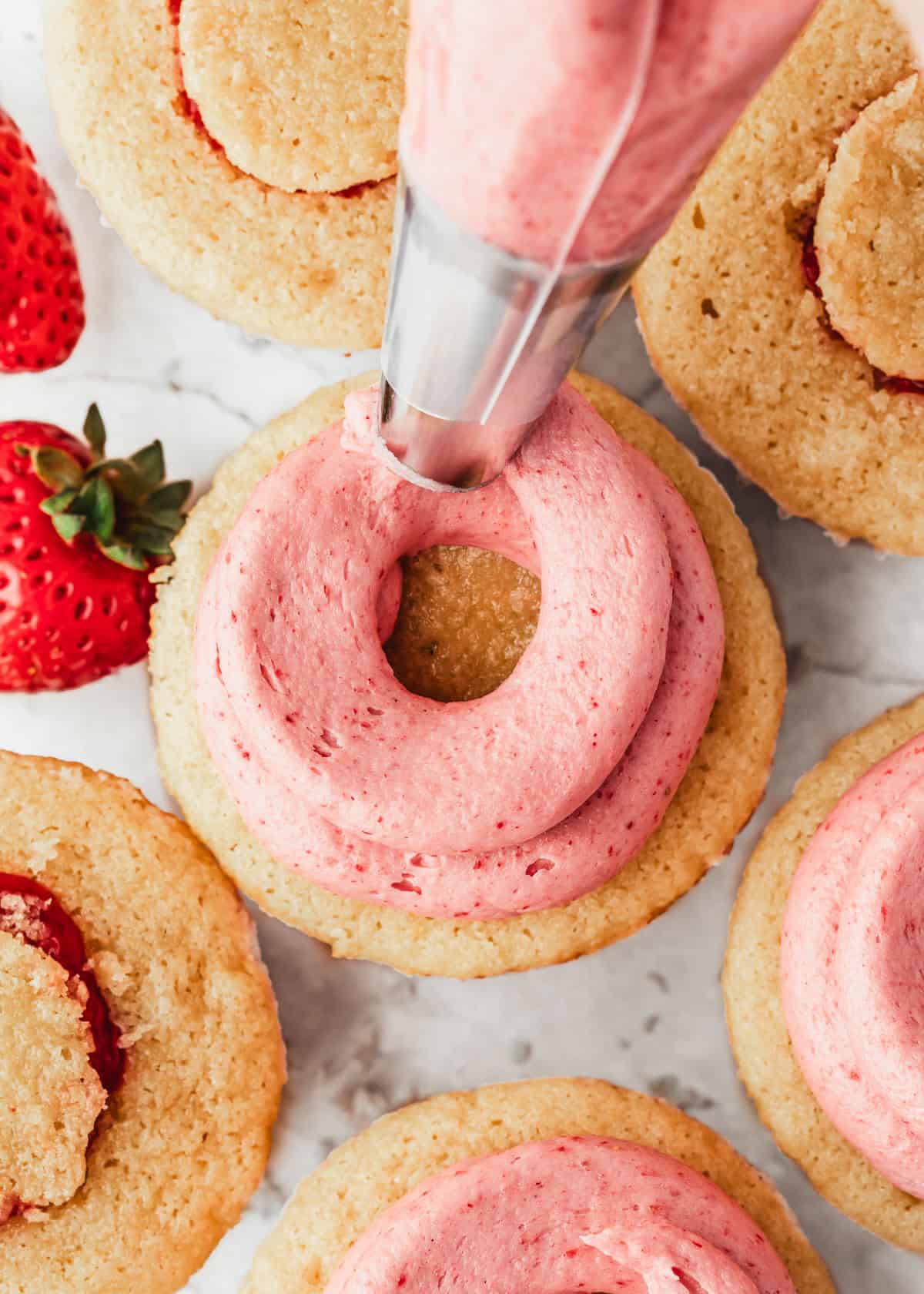 A piping bag piping small batch strawberry buttercream on cupcakes.