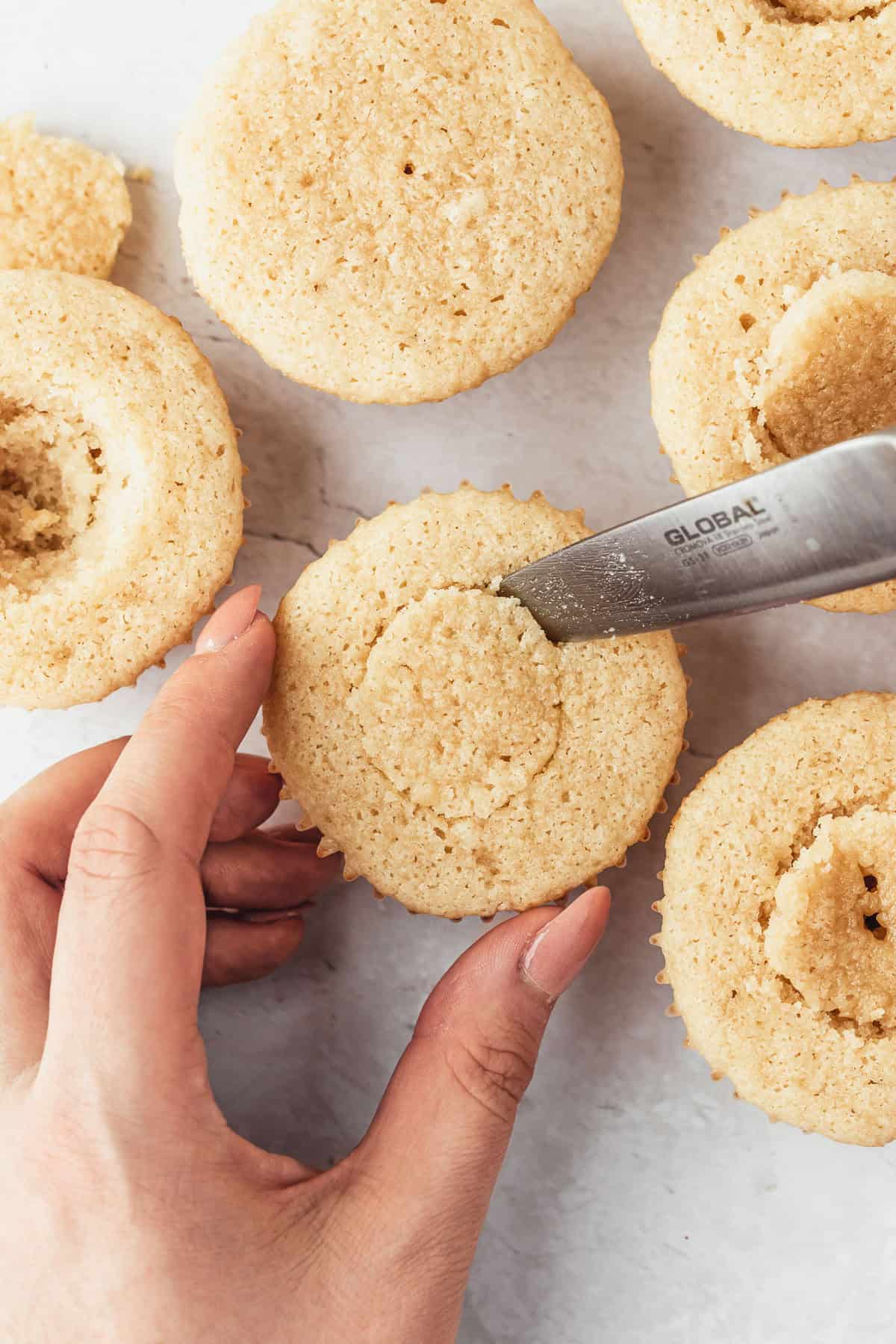 A hand using a knife to cut a hole in the center of a cupcake.