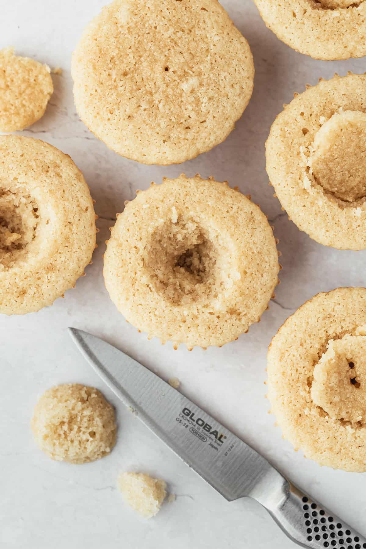 Rows of cupcakes with holes cut out of the middles on a white counter.