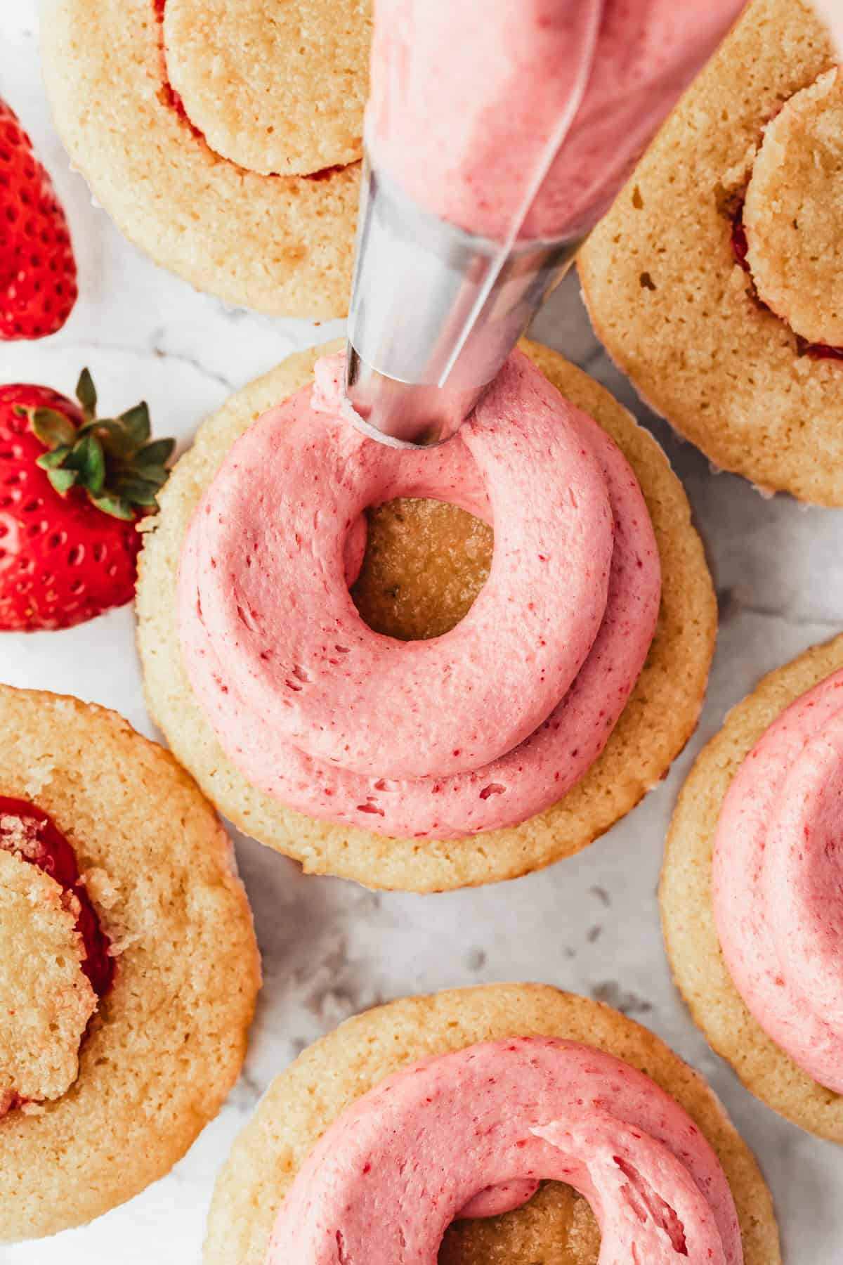 A piping bag frosting cupcakes on a white counter.
