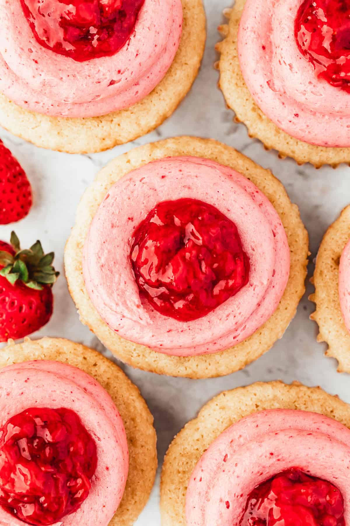 Rows of small batch strawberry filled cupcakes on a white counter.