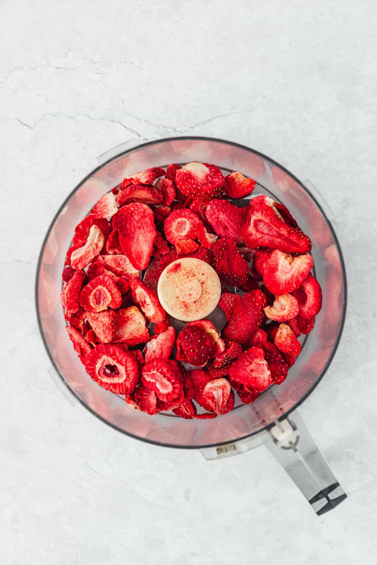 A food processor with freeze dried strawberries on a white counter.
