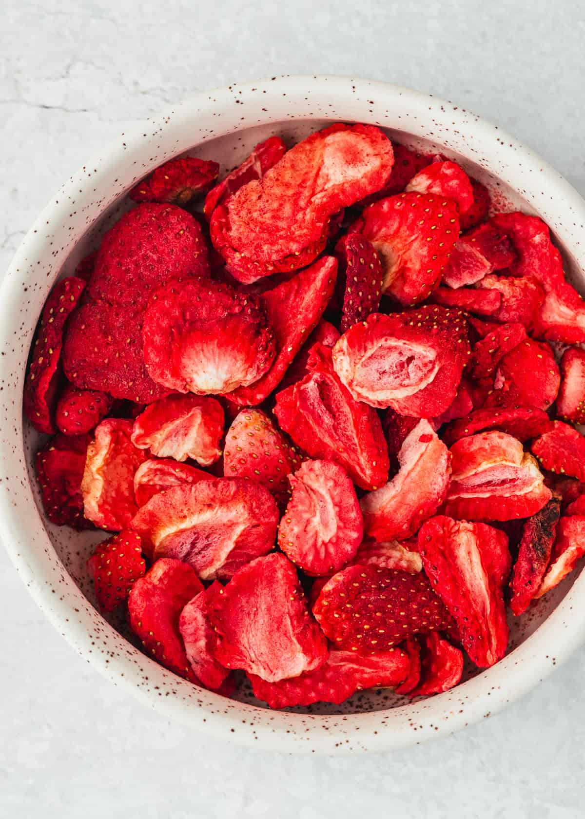 A white bowl of freeze dried strawberries on a white bowl.