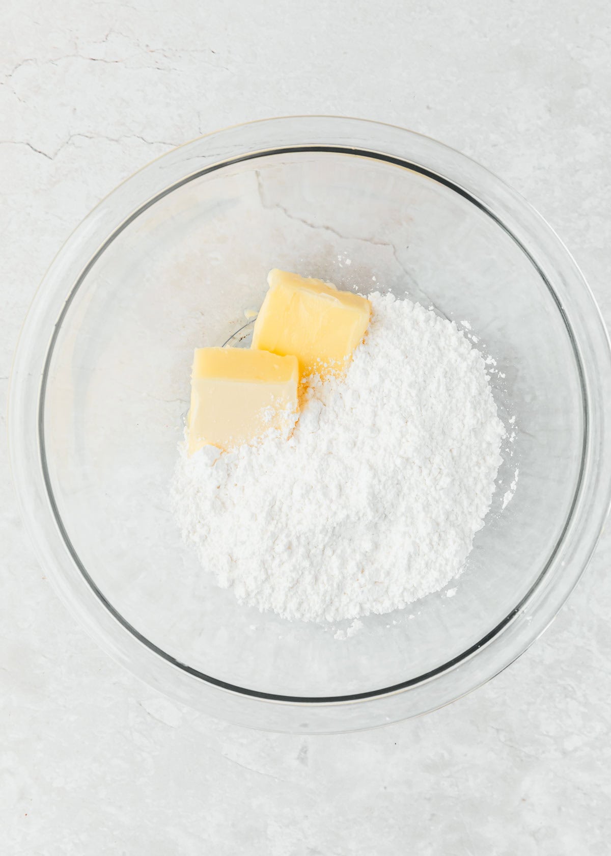A clear bowl of butter and powdered sugar on a white counter.
