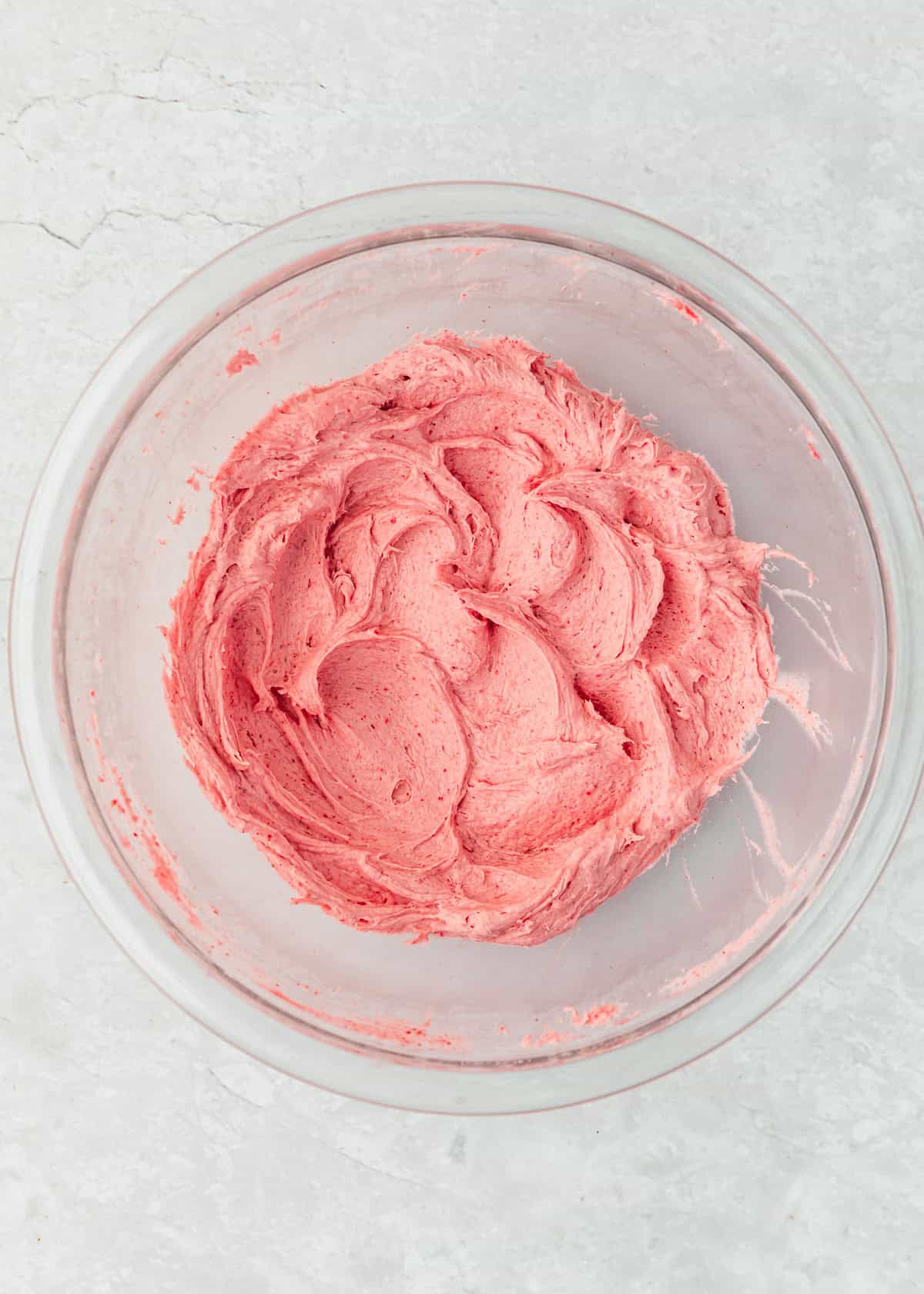A clear bowl of whipped small batch strawberry buttercream on a marble table.