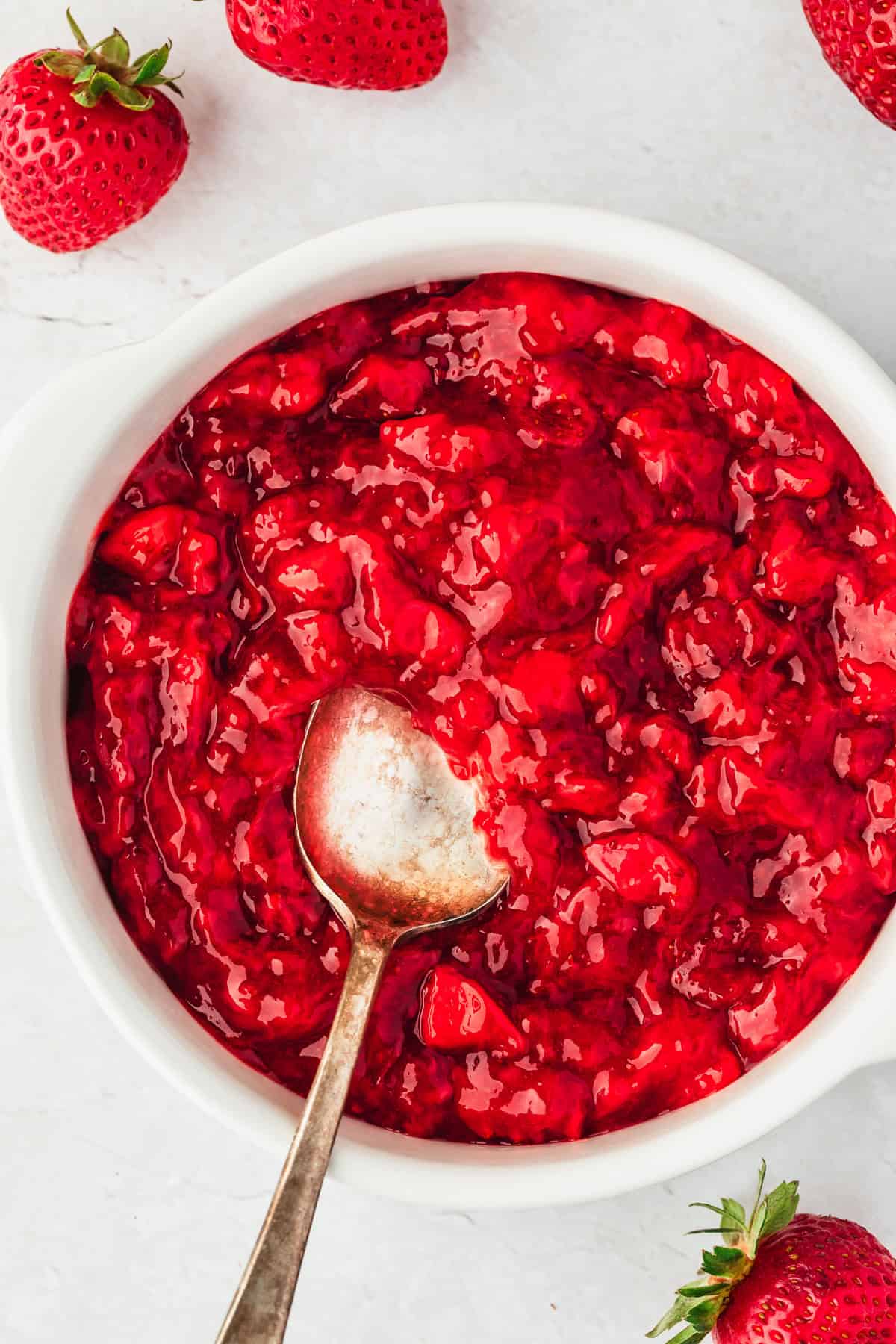 A white bowl of small batch strawberry filling for cake and cupcakes on a white counter next to fresh strawberries.