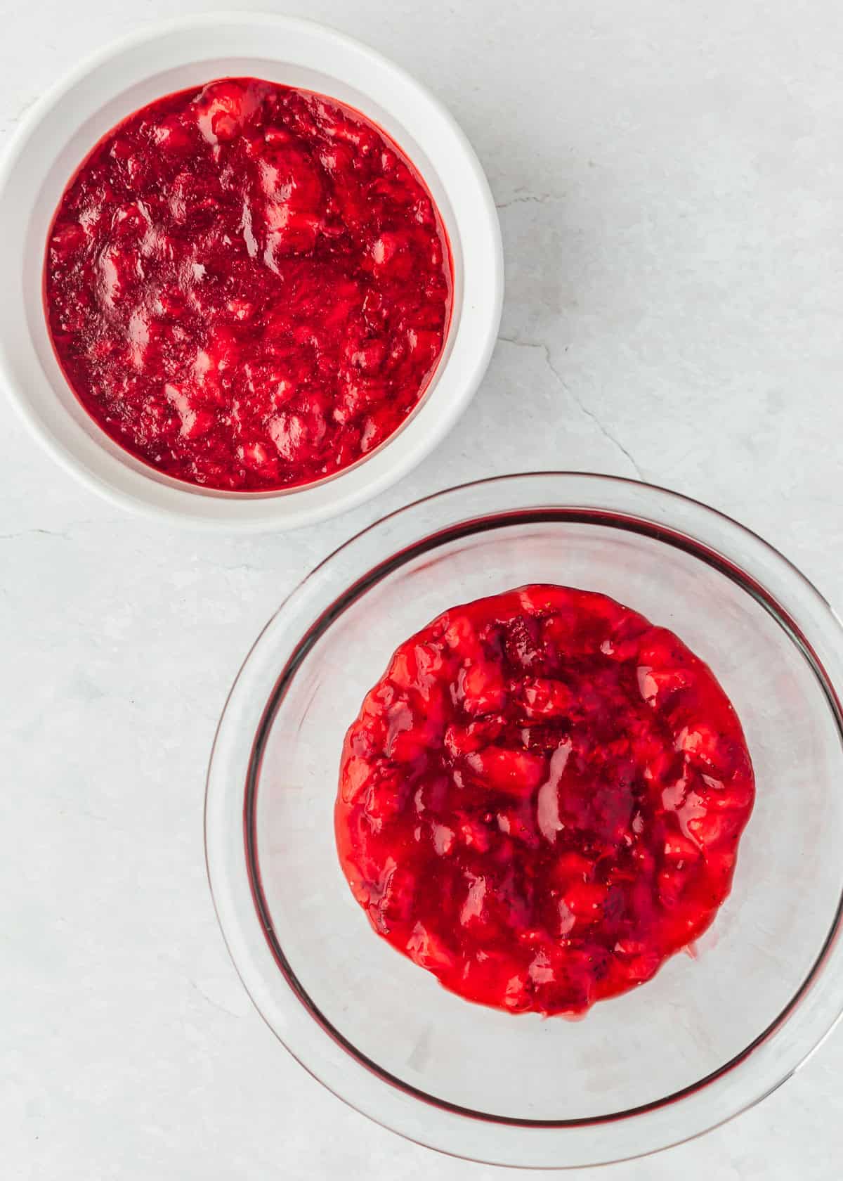Two bowls of small batch strawberry filling on a white marble table.