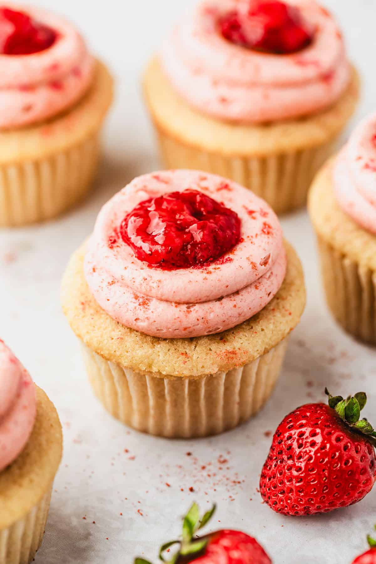Rows of small batch strawberry filled cupcakes on a white counter.