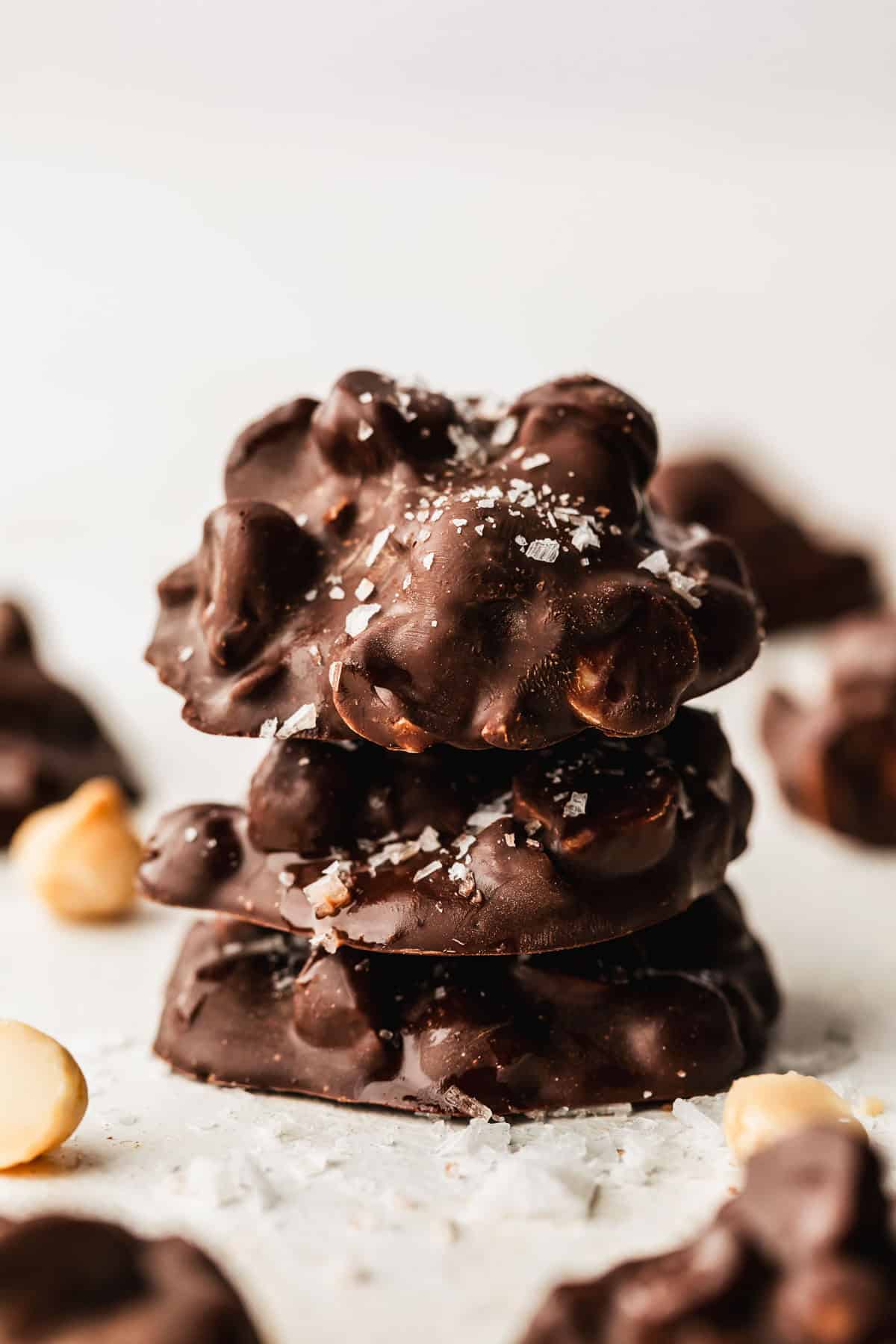 A stack of small batch macadamia nut chocolates next to macadamia nuts and more chocolates on parchment paper.