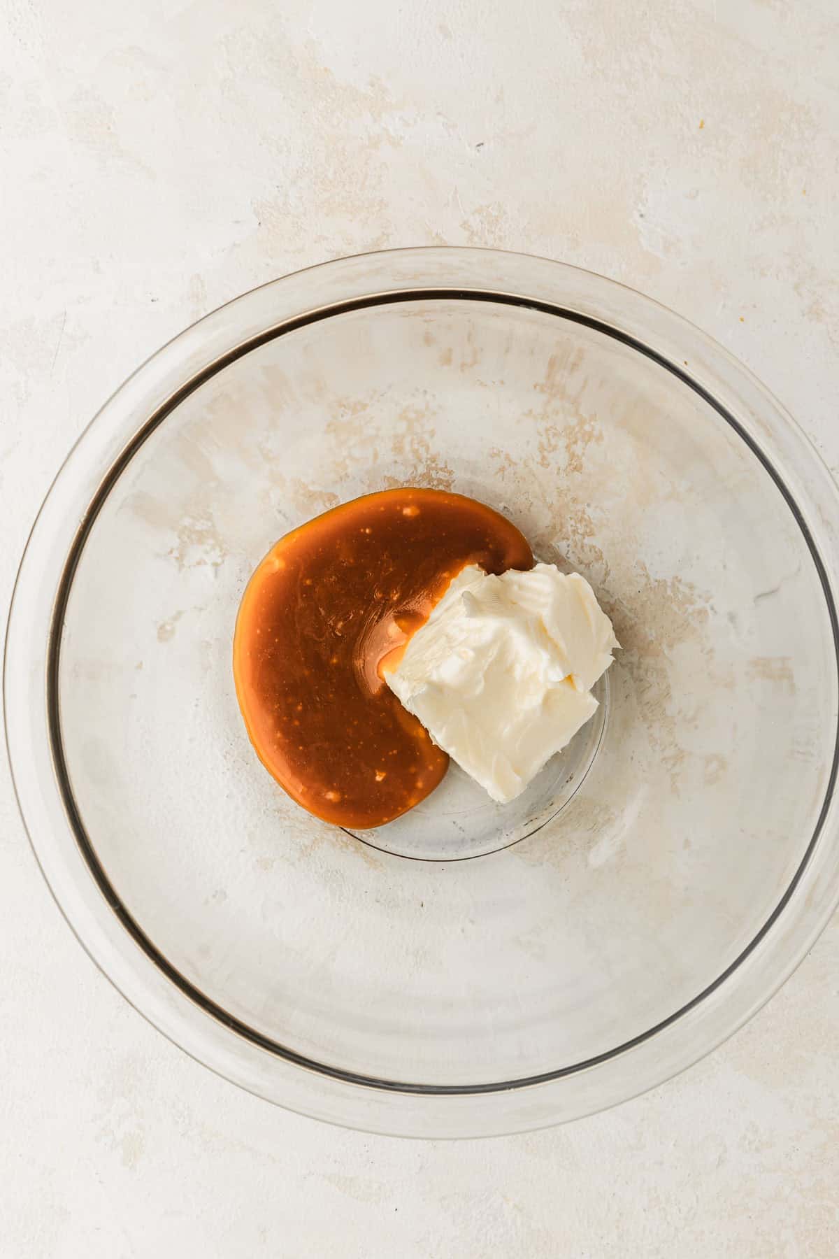 A clear bowl of butter and caramel sauce on a tan counter.