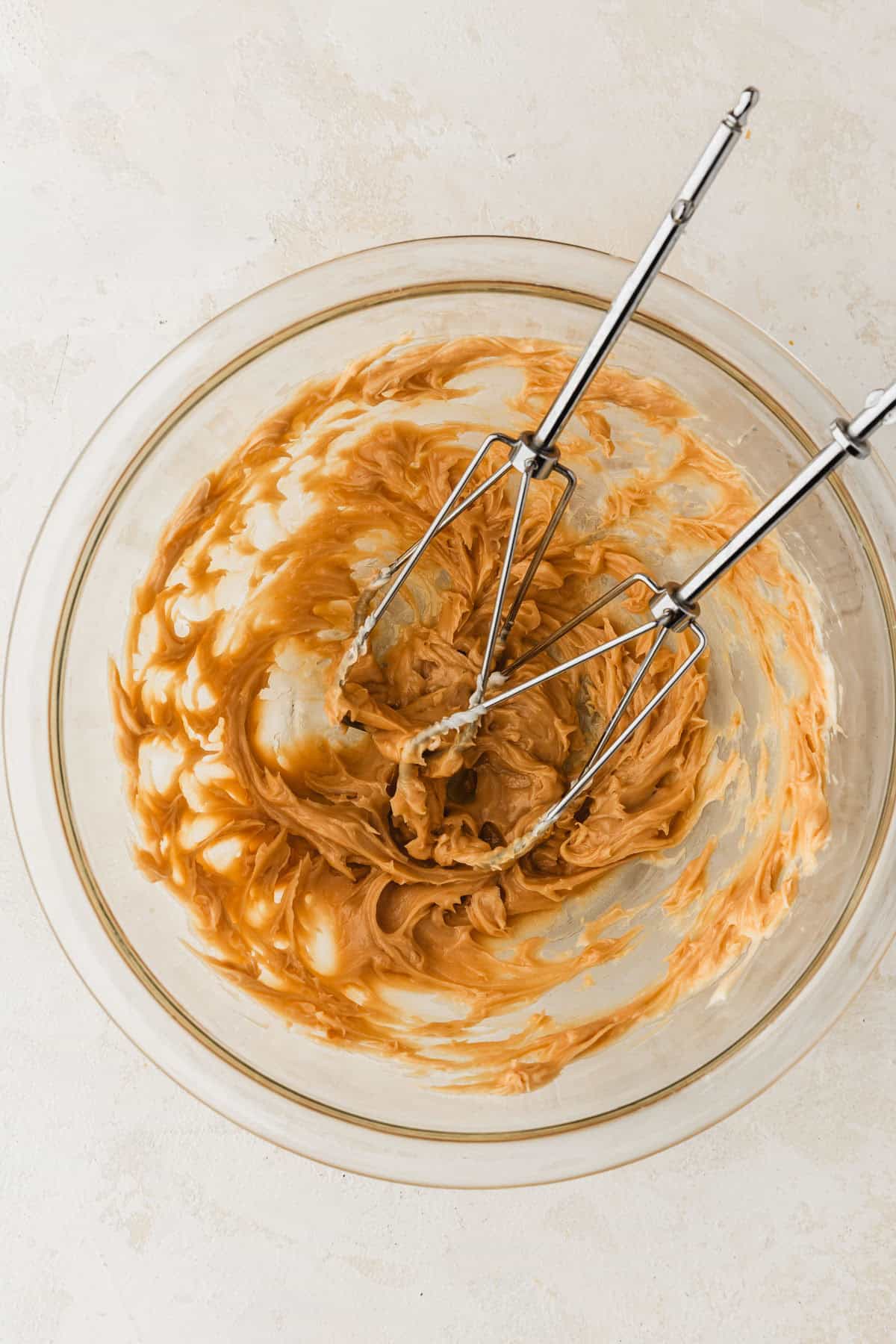 A clear bowl of whipped butter and caramel sauce with beaters.