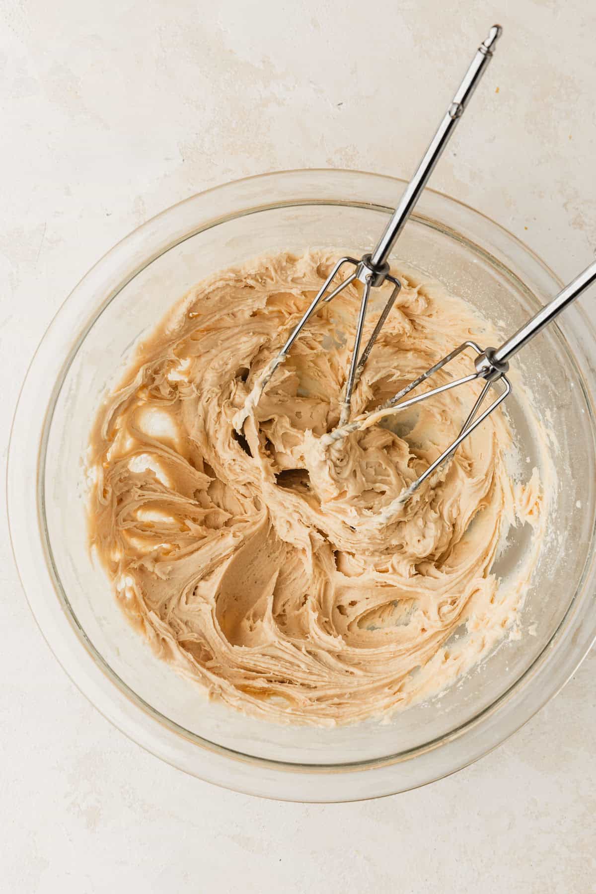 A clear bowl of frosting on a tan counter.