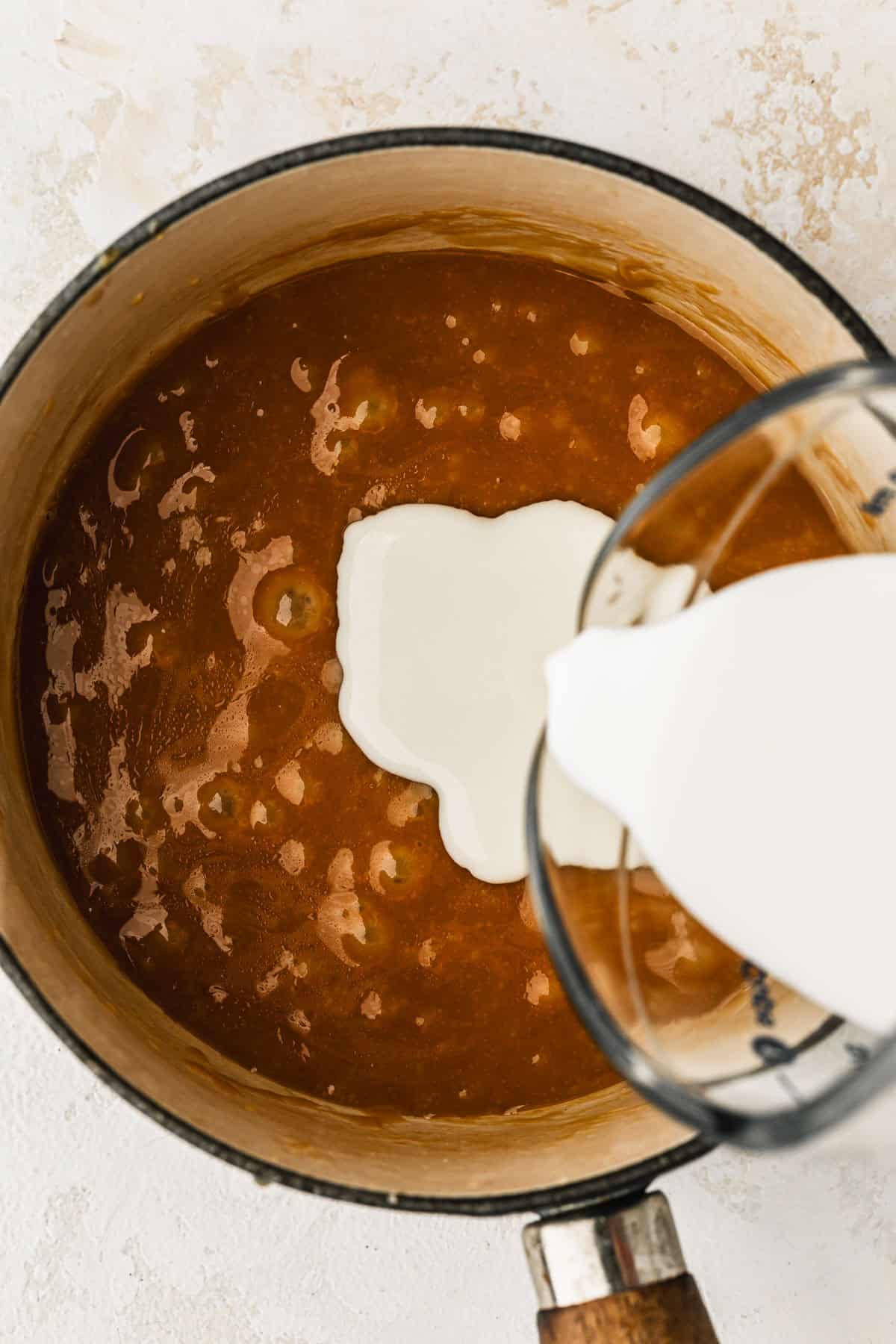 A white pot of small batch caramel sauce and cream.