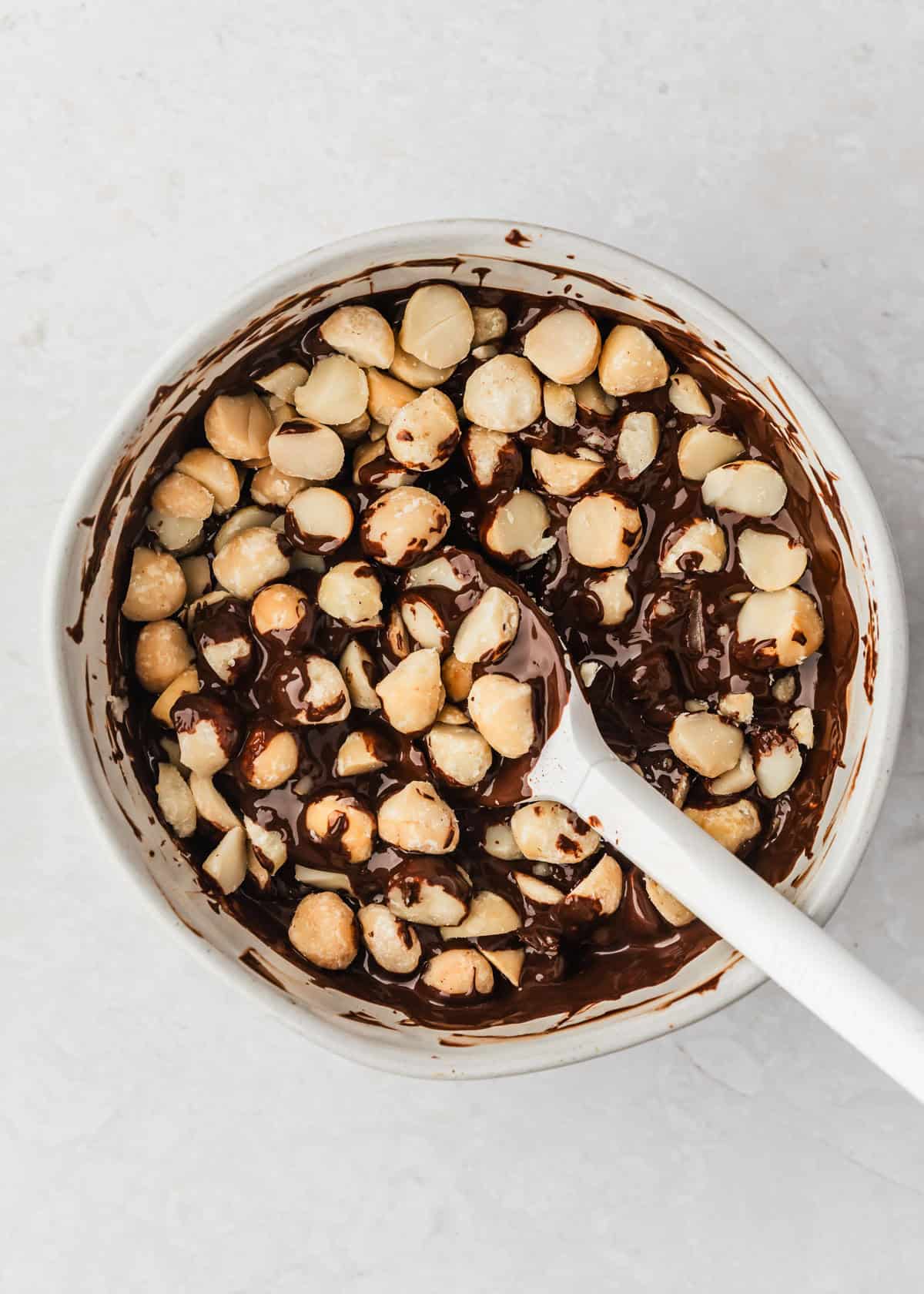 A white bowl of chocolate and nuts for small batch macadamia nut chocolates.