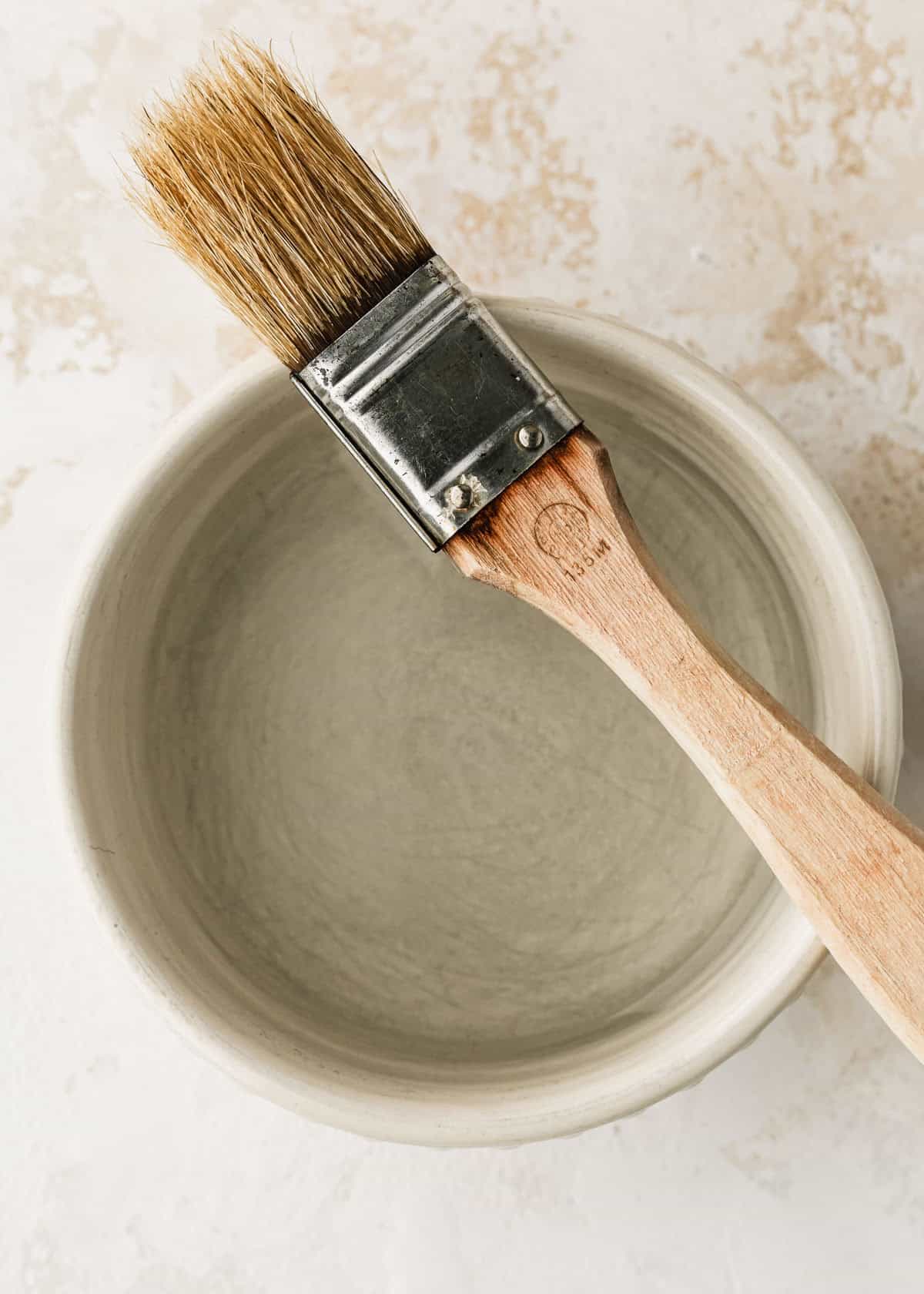 A white bowl of water with a pastry brush on a white counter.