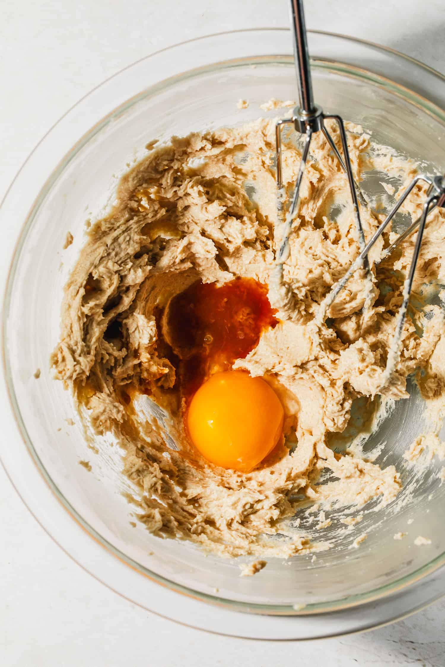 A glass bowl of creamed butter and sugar, an egg yolk, and vanilla extract.
