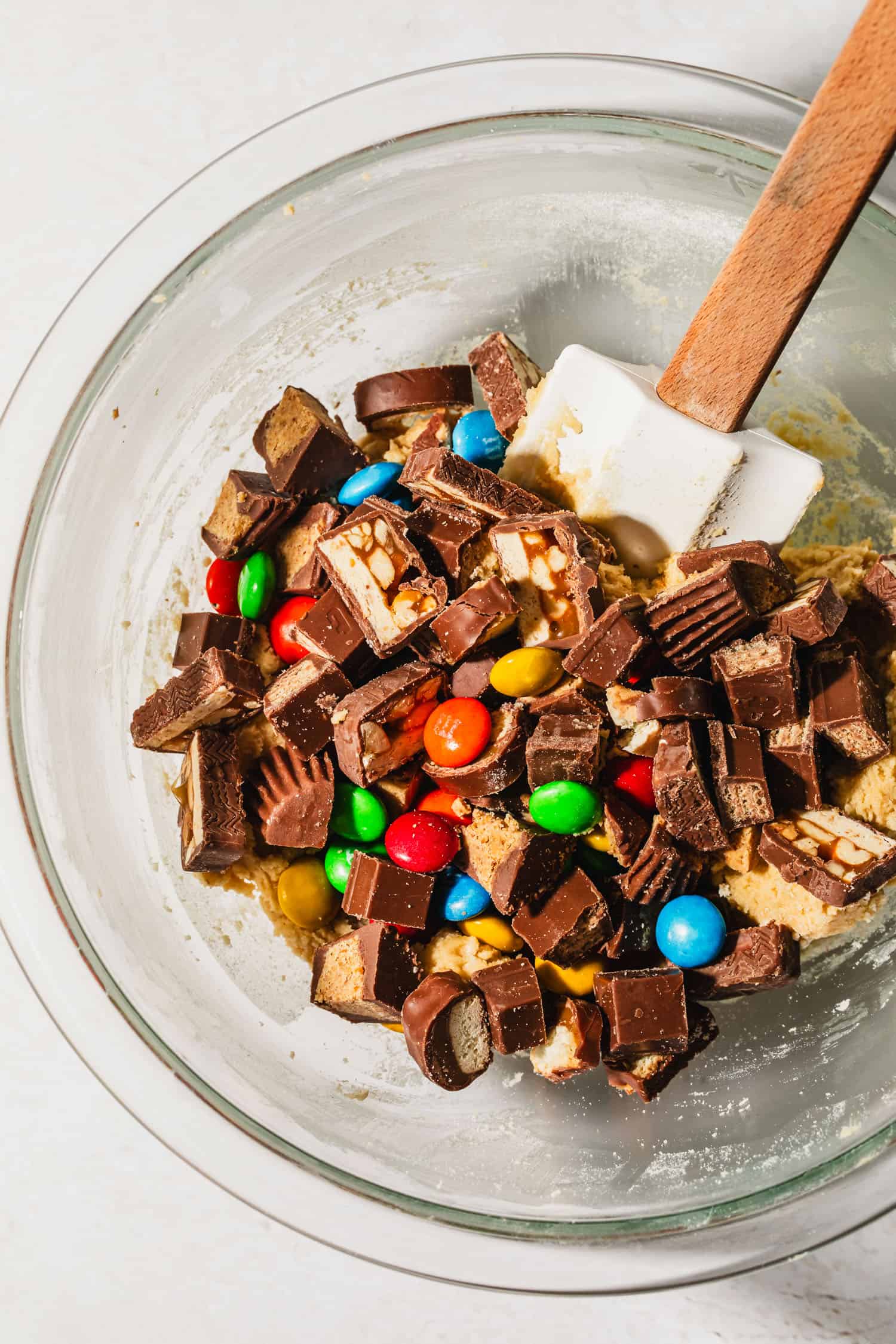 A glass bowl of cookie dough and chopped candy on a white counter.