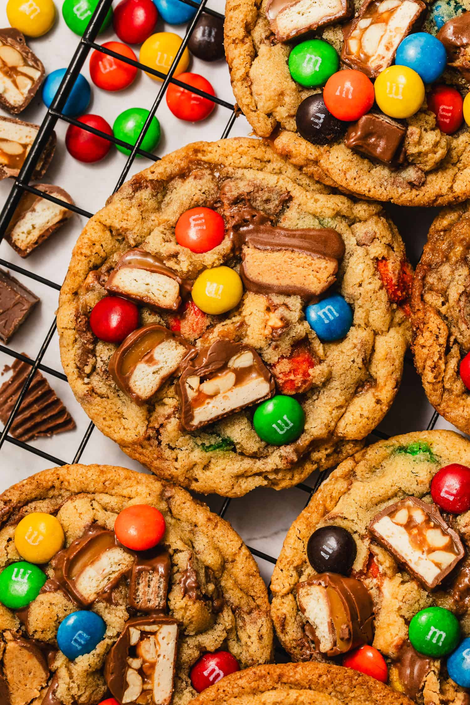 Rows of small batch leftover Halloween candy cookies on a black wire rack.