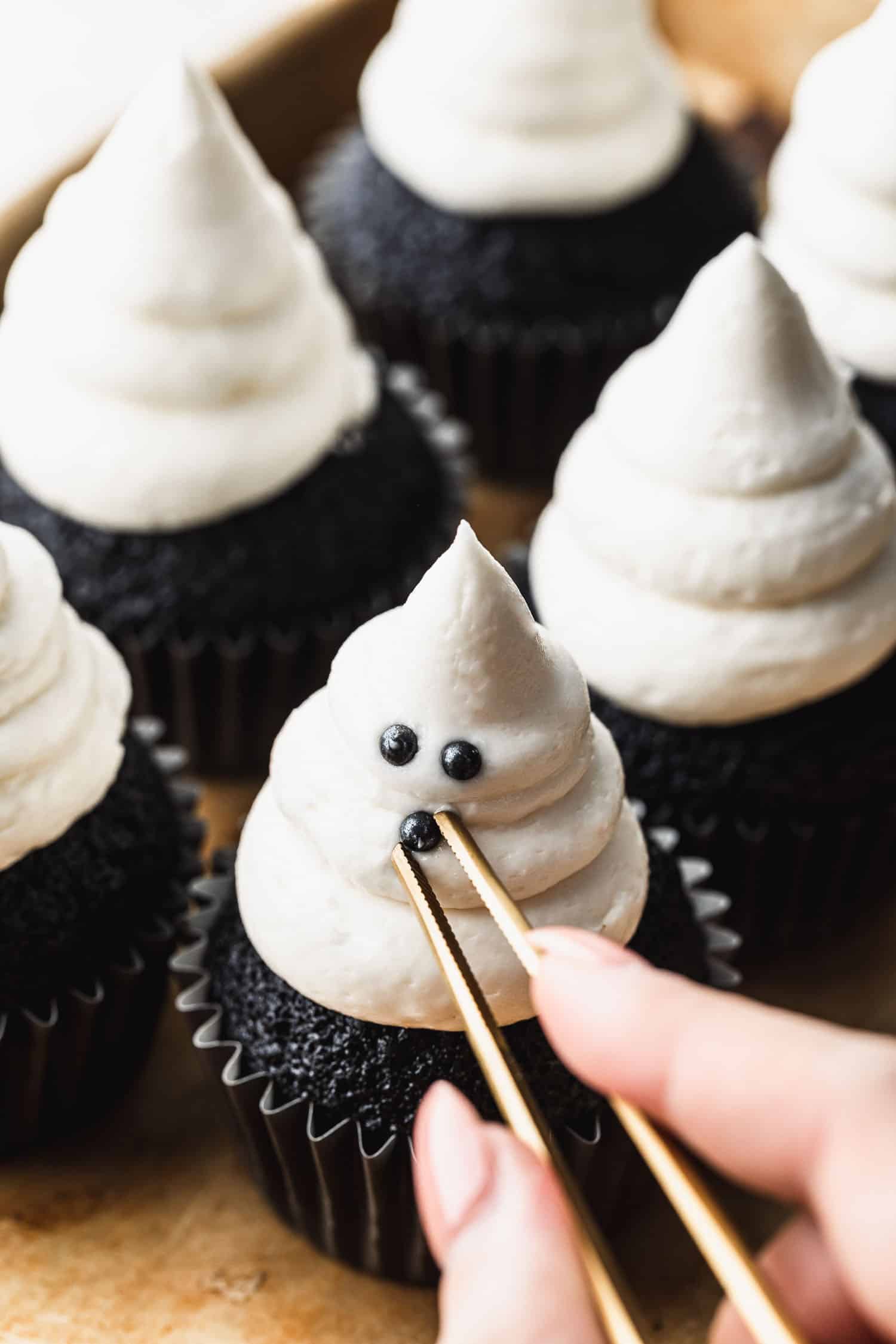 A hand using tweezers to add sprinkles to small batch ghost cupcakes.