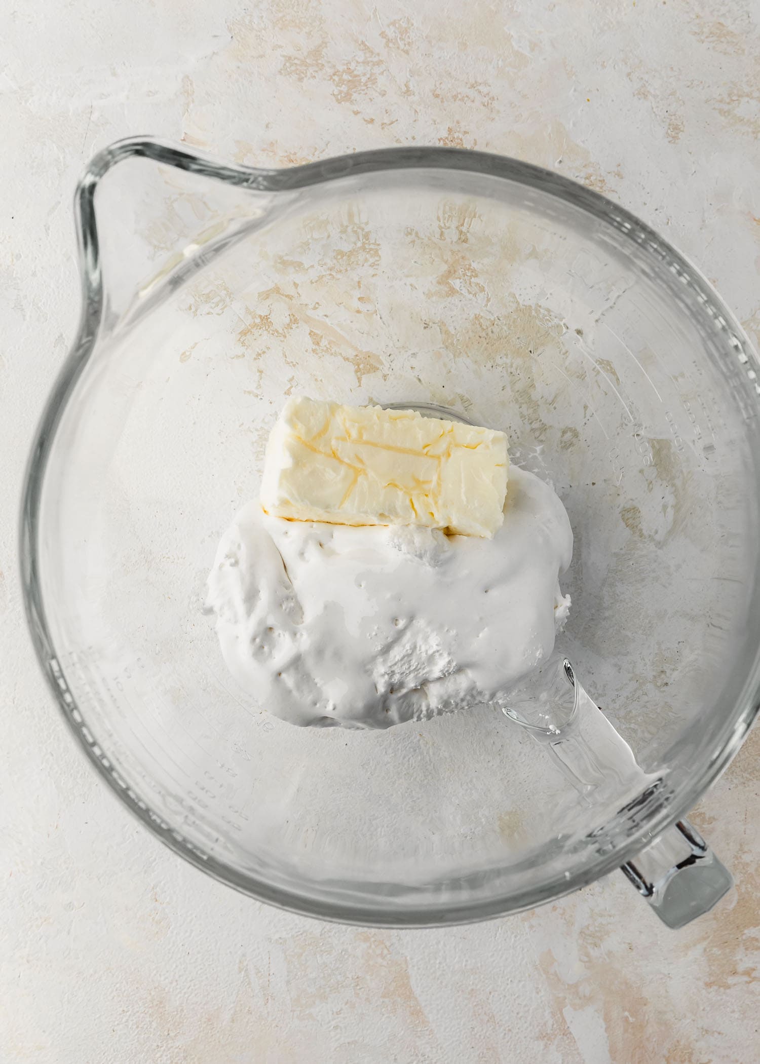 A clear bowl of butter and marshmallow cream on a tan counter.