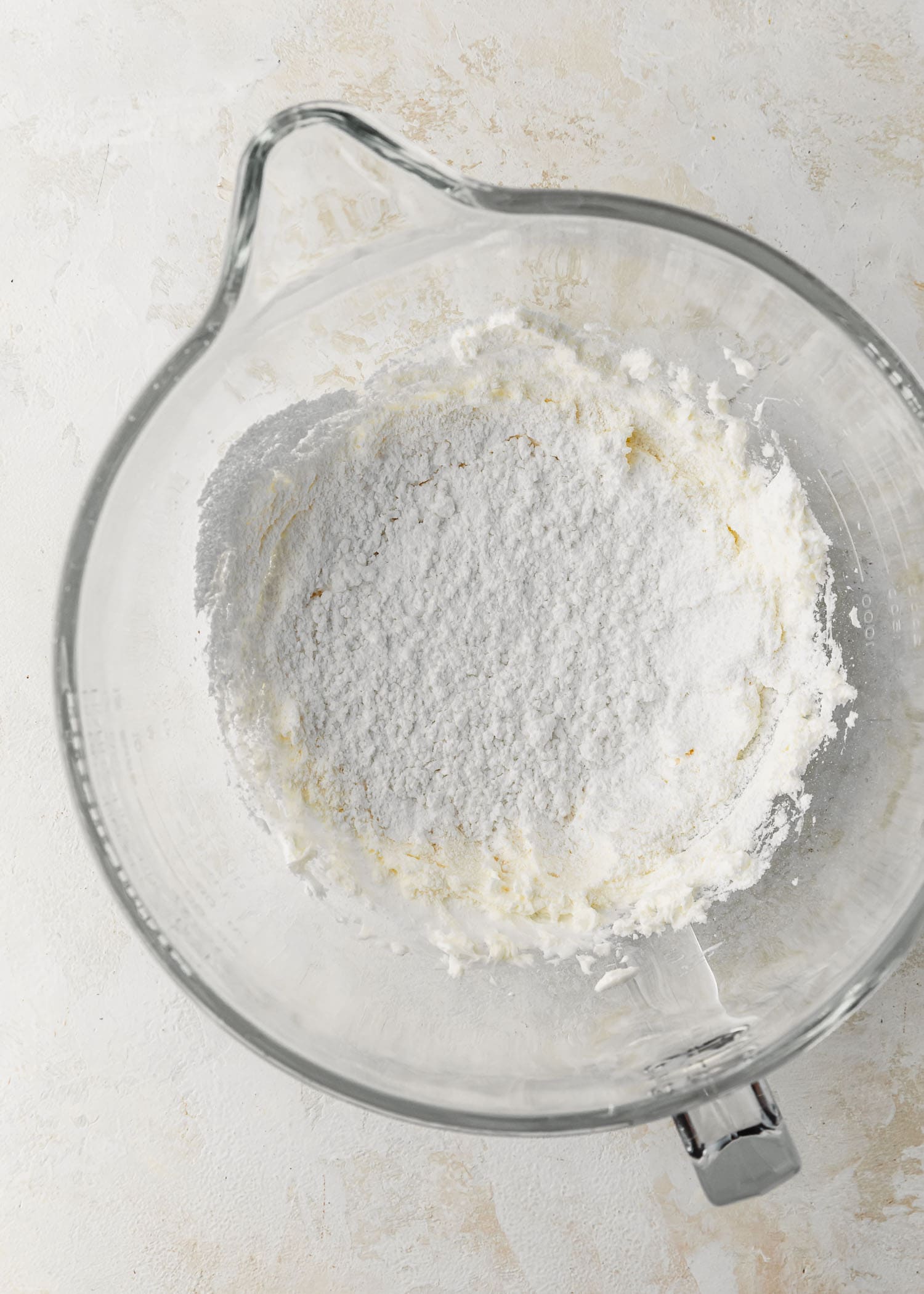 A clear bowl of butter, marshmallow fluff, and powdered sugar on a tan table.