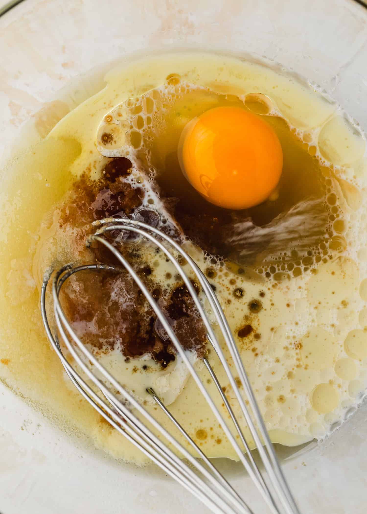 A clear bowl of oil, sugar, vanilla, and an egg.