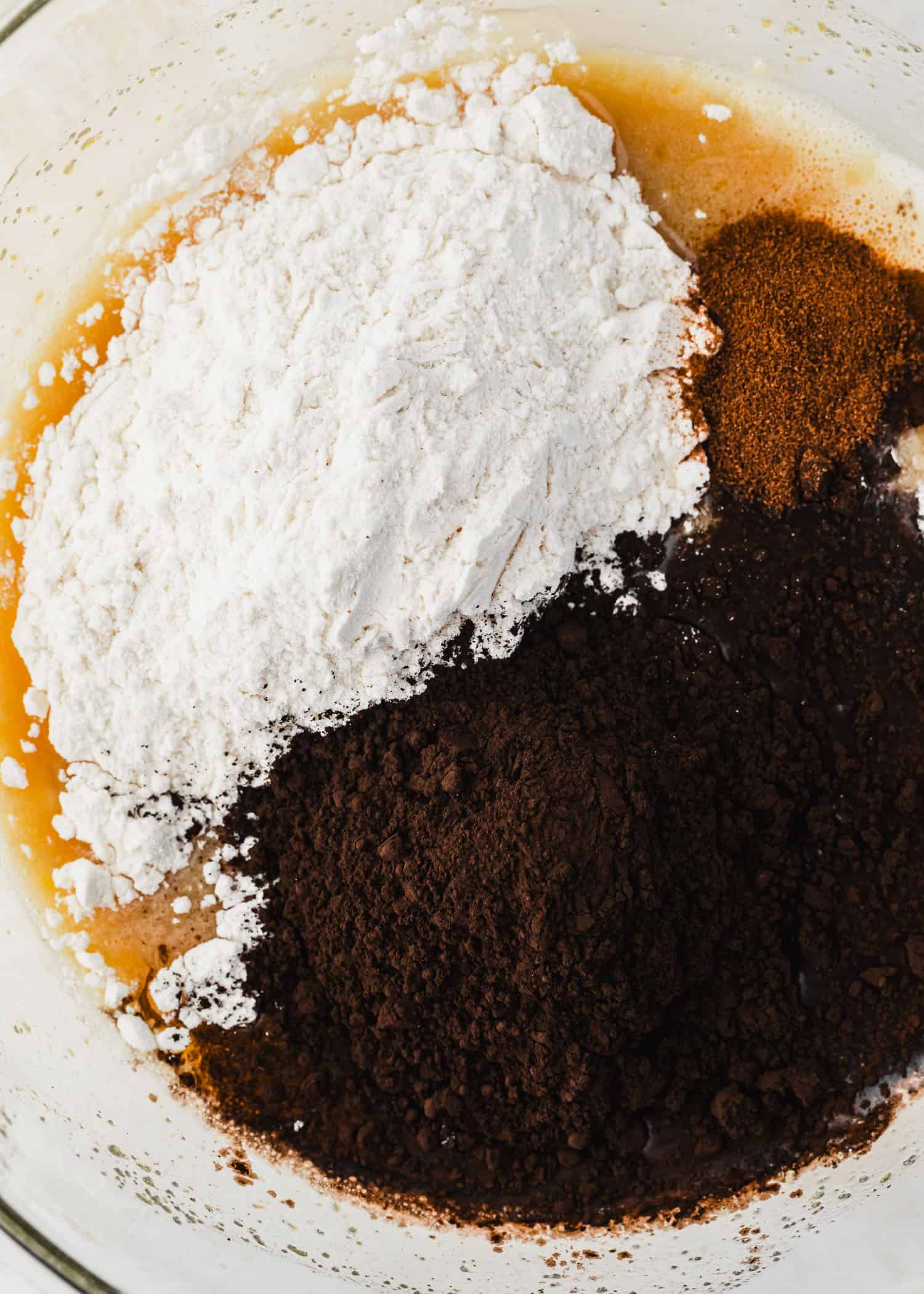 A clear bowl of flour, black cocoa powder, and instant coffee.