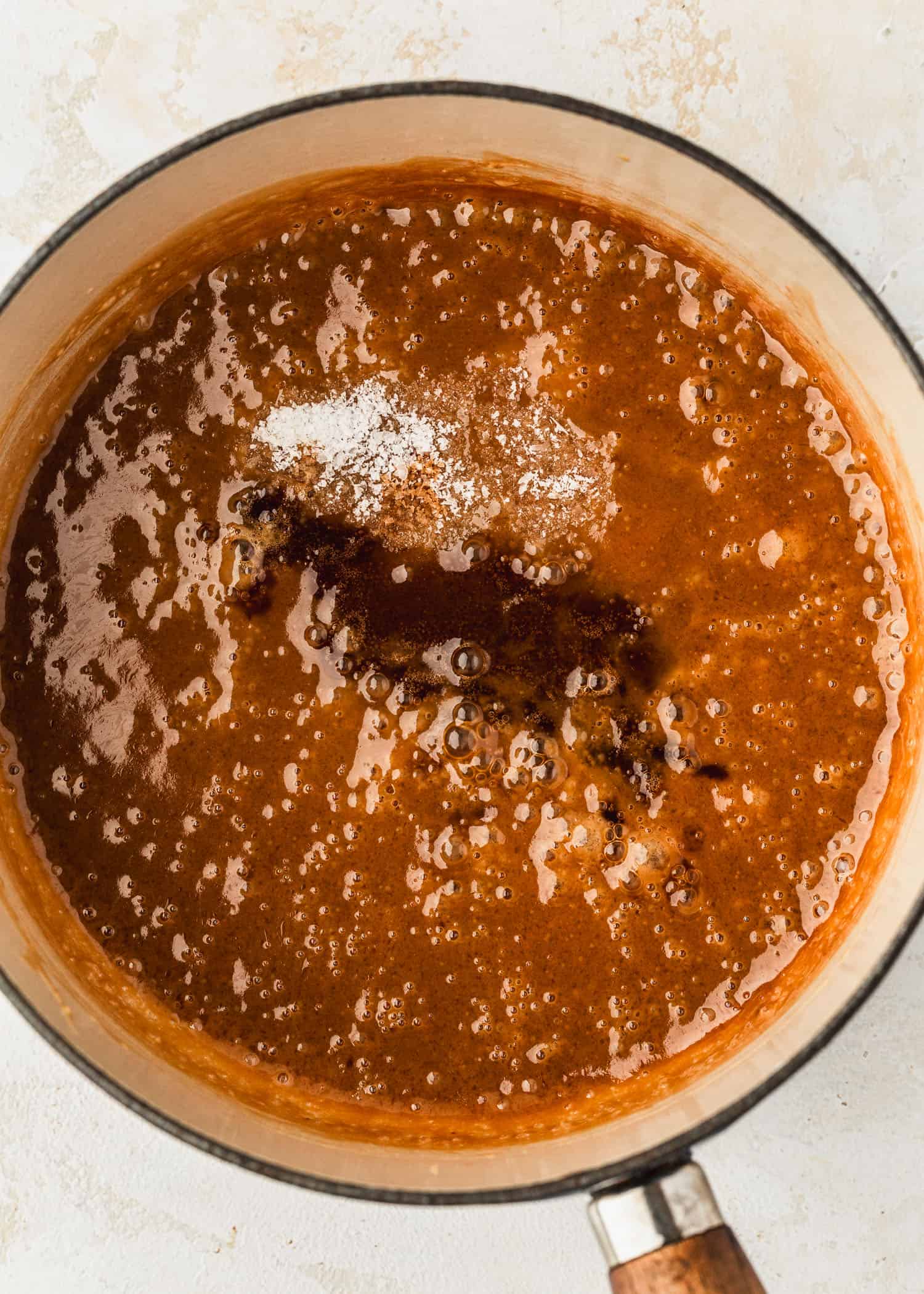 A white pot of small batch homemade butterscotch sauce on a tan counter.