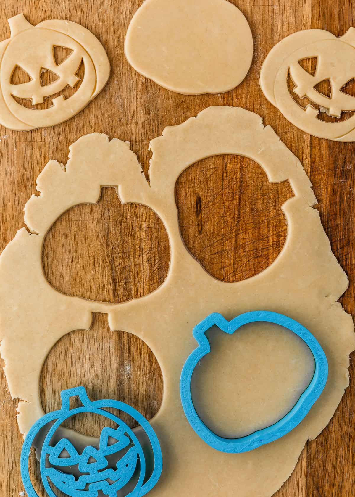 A pumpkin cookie cutter cutting shapes out of pie dough.