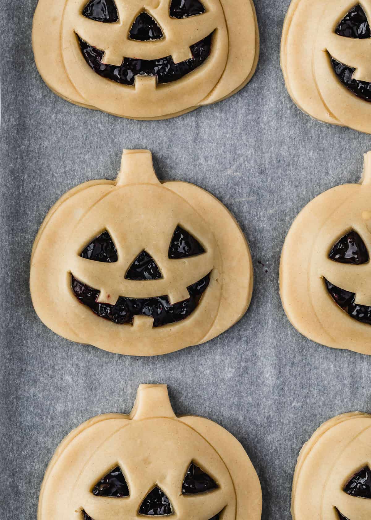 Raw Jack o'lantern hand pies on parchment paper.