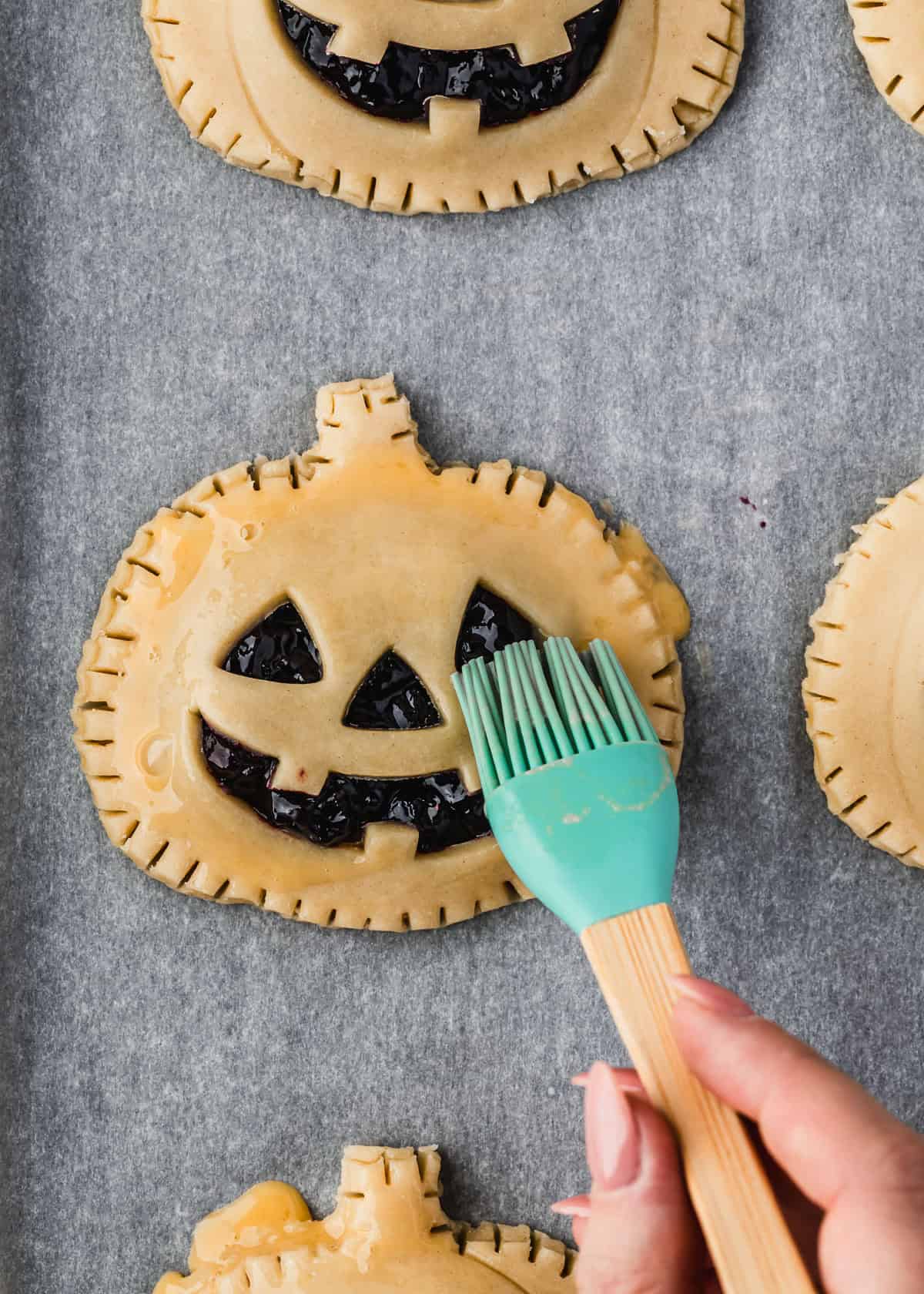 A hand using a pastry brush to brush pie dough with egg wash.