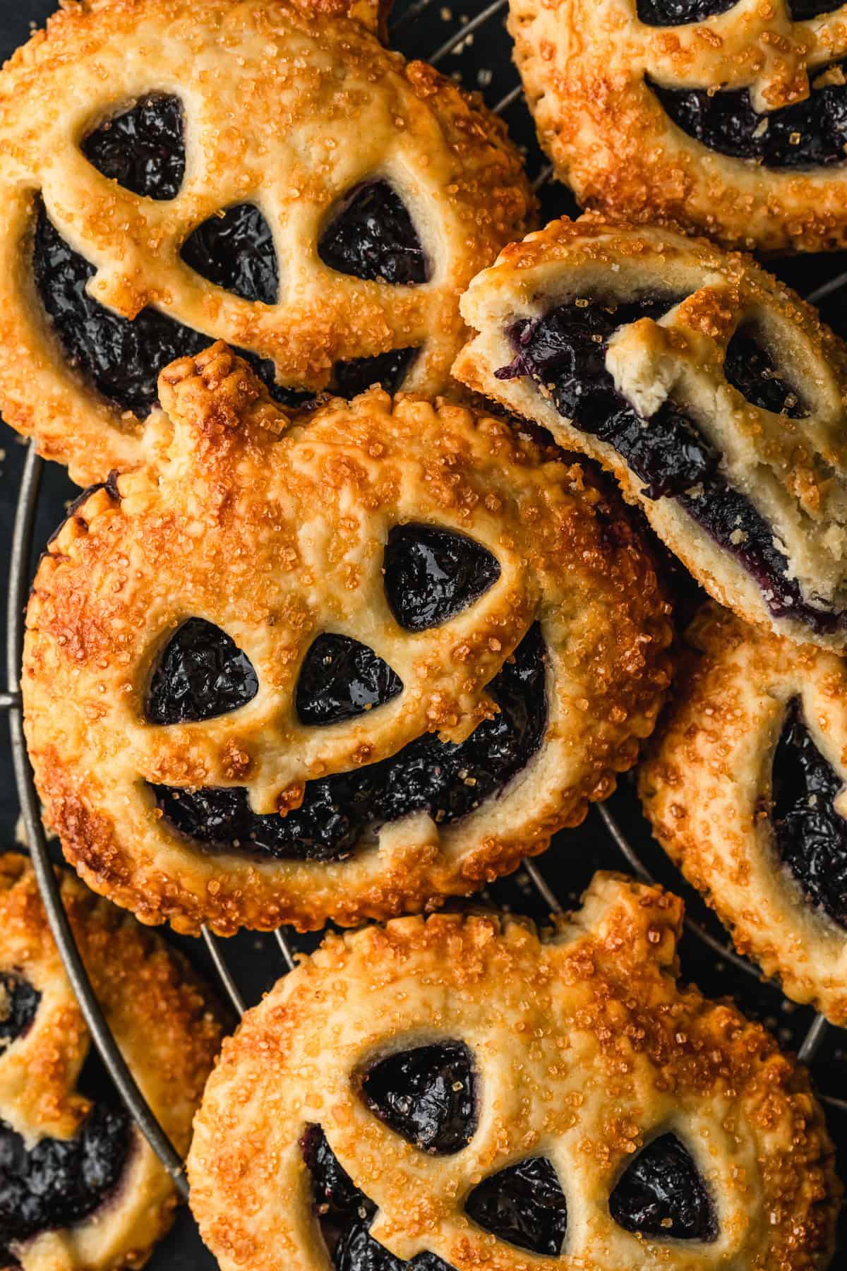 Rows of Halloween Jack o'lantern hand pies with blueberry filling on a wire rack.