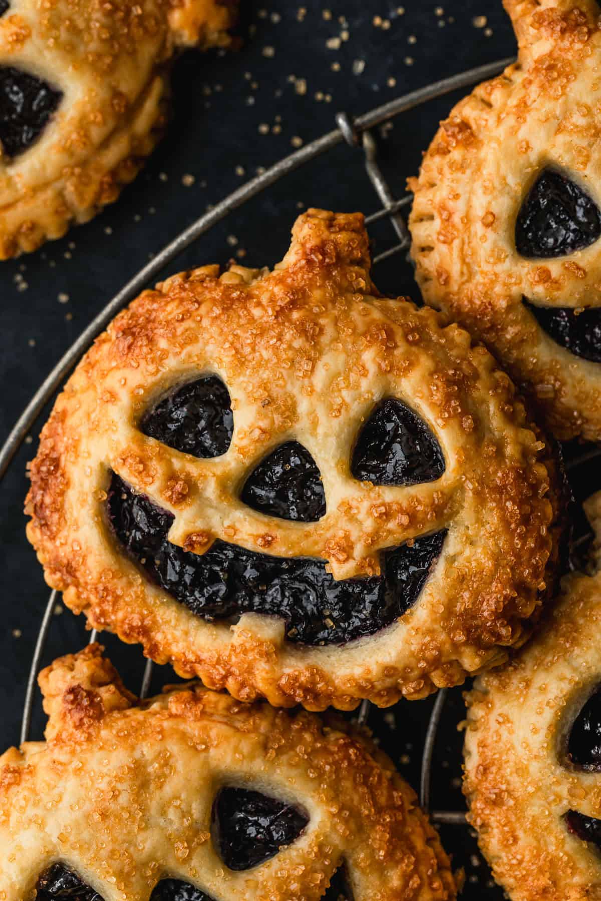 A wire rack of Jack o'lantern hand pies on a black counter.