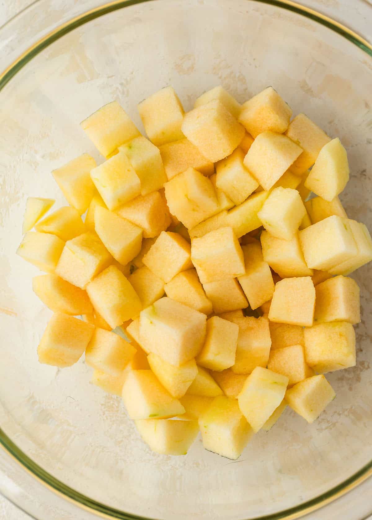 A clear bowl of diced apples on a tan counter.