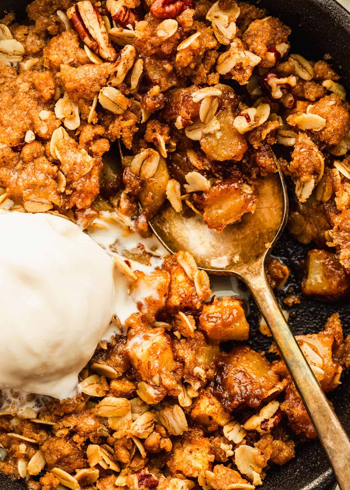 A single-serving apple crisp topped with ice cream in a black skillet.
