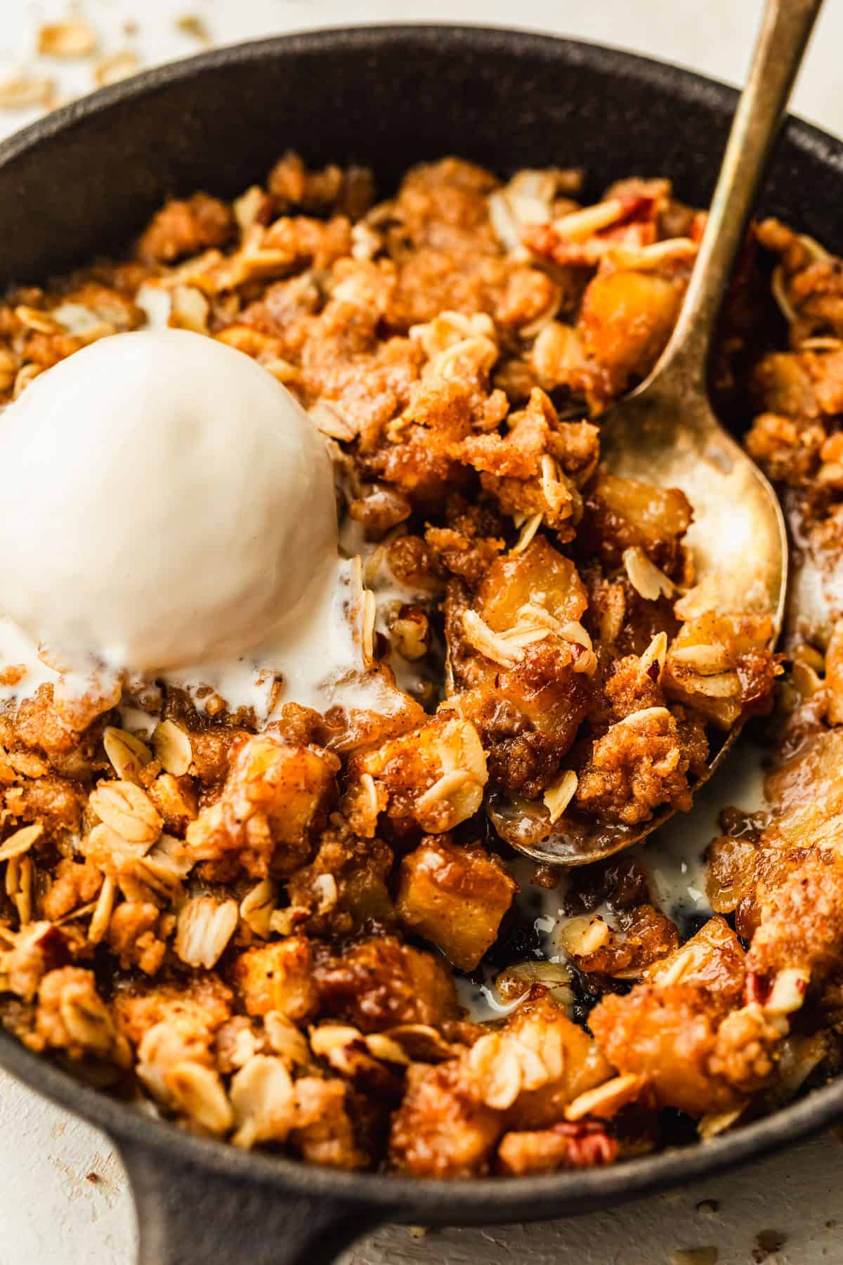 A black skillet of a single-serving apple crisp topped with ice cream.